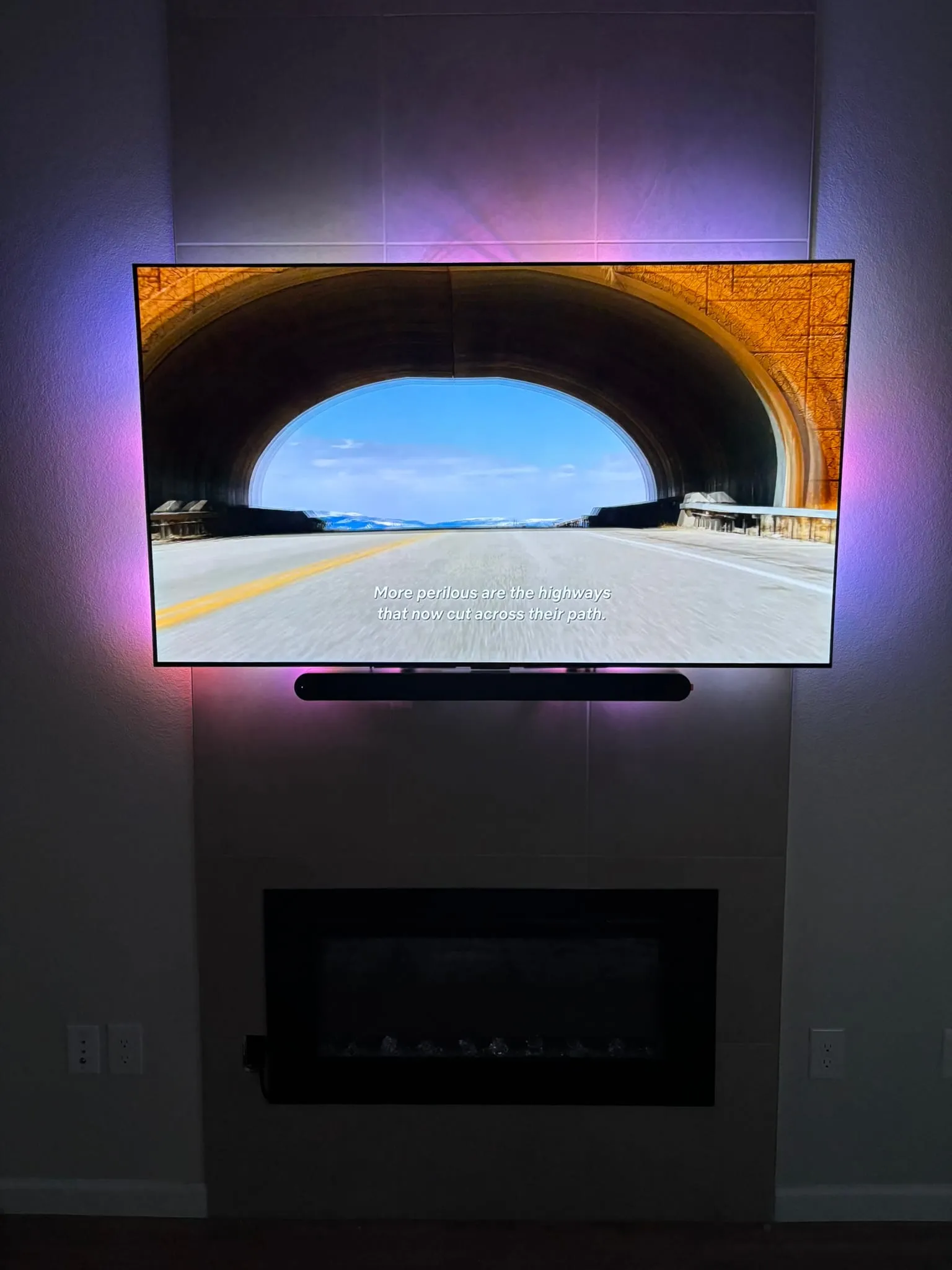 Large TV mounted above a tiled fireplace with a soundbar below and no visible cables